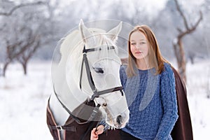 Young teenage girl with white horse in winter park