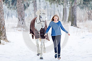 Young teenage girl with white horse in winter park