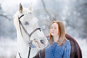 Young teenage girl with white horse in winter park