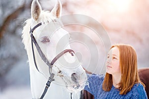 Young teenage girl with white horse in winter park