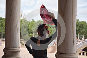 Young teenage woman with black dance dress and pink carnations in her hair, with red fan dancing flamenco. Flamenco concept, dance