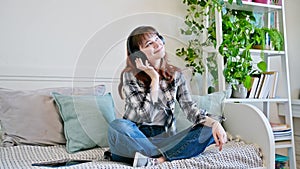 Young teenage woman in headphones listening to music, relaxing at home