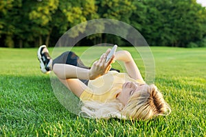 Young teenage woman lying on green grass using smartphone