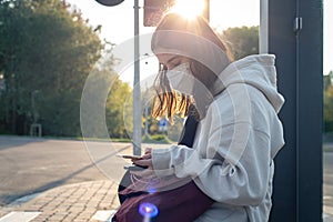 A young teenage woman is waiting for a bus at a bus stop early in the morning.