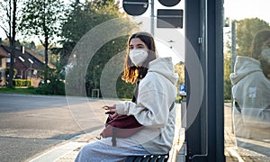 A young teenage woman is waiting for a bus at a bus stop early in the morning.