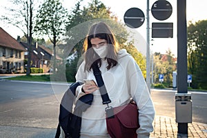 A young teenage woman is waiting for a bus at a bus stop early in the morning.