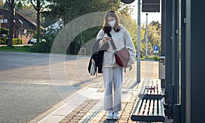 A young teenage woman is waiting for a bus at a bus stop early in the morning.