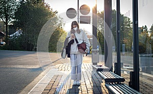 A young teenage woman is waiting for a bus at a bus stop early in the morning.