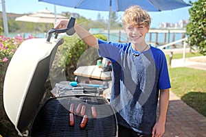 Young Teenaged Boy Cooking Hotdogs on the Grill for a Picnic for his Family