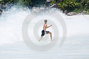 Young teenager boy enjoys summer holiday in sea. The kid runs away from huge wave.