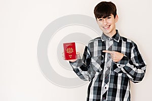 Young teenager boy holding Malaysia passport looking positive and happy standing and smiling with a confident smile against white