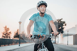 Young teenager boy in protection helmet riding bike and doing sports in park next to trees