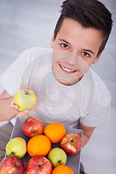 Young teenager boy sitting on the floor with a plate of fruits