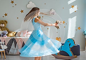 Young teenager brunette girl with long hair in blue dress in her bedroom play with childrenÃ¢â‚¬â„¢s toy