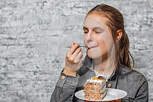 Young teenager brunette girl with long hair eating slice cake dessert on gray wall background