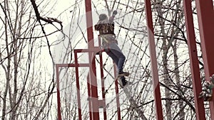 Young teenager climber walks by pendant log bridge on high ropes course in extreme park