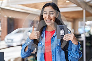 Young teenager girl holding canada passport smiling happy and positive, thumb up doing excellent and approval sign