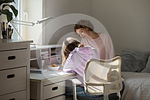 Young teenager girl preparing homework with caring mother.