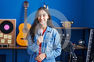 Young teenager girl singing song using microphone looking positive and happy standing and smiling with a confident smile showing