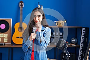 Young teenager girl singing song using microphone serious face thinking about question with hand on chin, thoughtful about