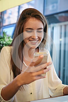 Young teenager girl sitting in cafe and using smart phone.