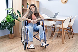 Young teenager girl sitting on wheelchair at the living room looking positive and happy standing and smiling with a confident