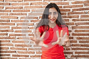 Young teenager girl standing over bricks wall afraid and terrified with fear expression stop gesture with hands, shouting in shock