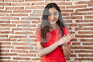 Young teenager girl standing over bricks wall clapping and applauding happy and joyful, smiling proud hands together