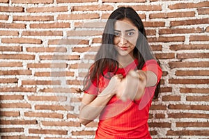 Young teenager girl standing over bricks wall punching fist to fight, aggressive and angry attack, threat and violence