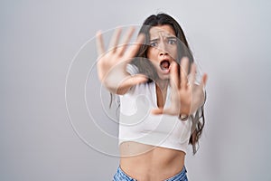 Young teenager girl standing over white background afraid and terrified with fear expression stop gesture with hands, shouting in