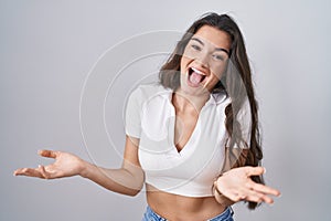 Young teenager girl standing over white background smiling cheerful with open arms as friendly welcome, positive and confident