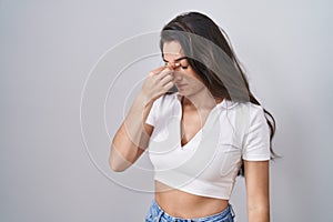 Young teenager girl standing over white background tired rubbing nose and eyes feeling fatigue and headache