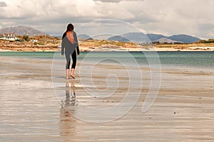 Young teenager girl walking on a warm sand of Gurteen beach, county Galway, Ireland. Warm sunny day. Cloudy sky. Outdoor activity