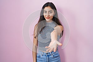 Young teenager girl wearing casual striped t shirt smiling friendly offering handshake as greeting and welcoming