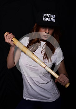 Young teenager girl in a white shirt, black cap, posing with baseball bat. play of light and shadows