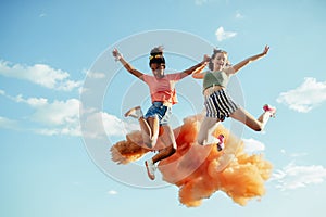 Young teenager girls friends jumping high. Having fun outdoors in city, standing on concrete wall.