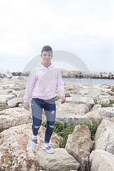 Young teenager male walking over rocks breakwaters while looking at camera