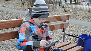 Young teenager playing game on smartphone on the bench outside.