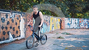 Young teenager rides and then pulls up a BMX bike. Copy space. Slowmo. Slow motion. Crop. 4K.