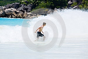 Young, teenager slender boy runs away from splashing wave at beach of Seychelles