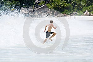 Young, teenager slender boy runs away from splashing wave at beach of Seychelles