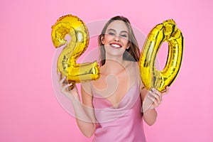 Young teenager smiling girl holds gold foil balloon on pink background. BIRTHDAY PARTY concept