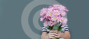 A young teenager in a striped t-shirt holding a bouquet of beautiful chrysanthemums covering his face. Isolated gray background,