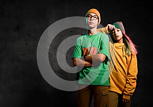 Young teens boy and girl in green and yellow stylish casual clothing and hats standing and looking at camera over dark background