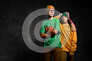 Young teens boy and girl in green and yellow stylish casual clothing and hats standing and looking at camera over dark background