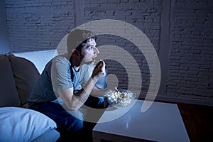 Young television addict man sitting on home sofa watching TV and eating popcorn