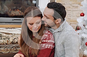 Young tender couple in comfy sweaters sitting near fireplace in