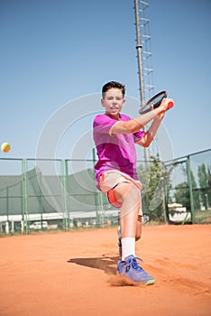 Young tennis player playing backhand and glide on a sunny day.