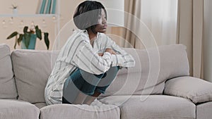 Young tense depressed sad woman sitting on sofa hugging knees thinking about personal problems frustrated stressed girl