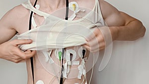 Young thin man puts on shirt. holter monitor is attached to chest underneath